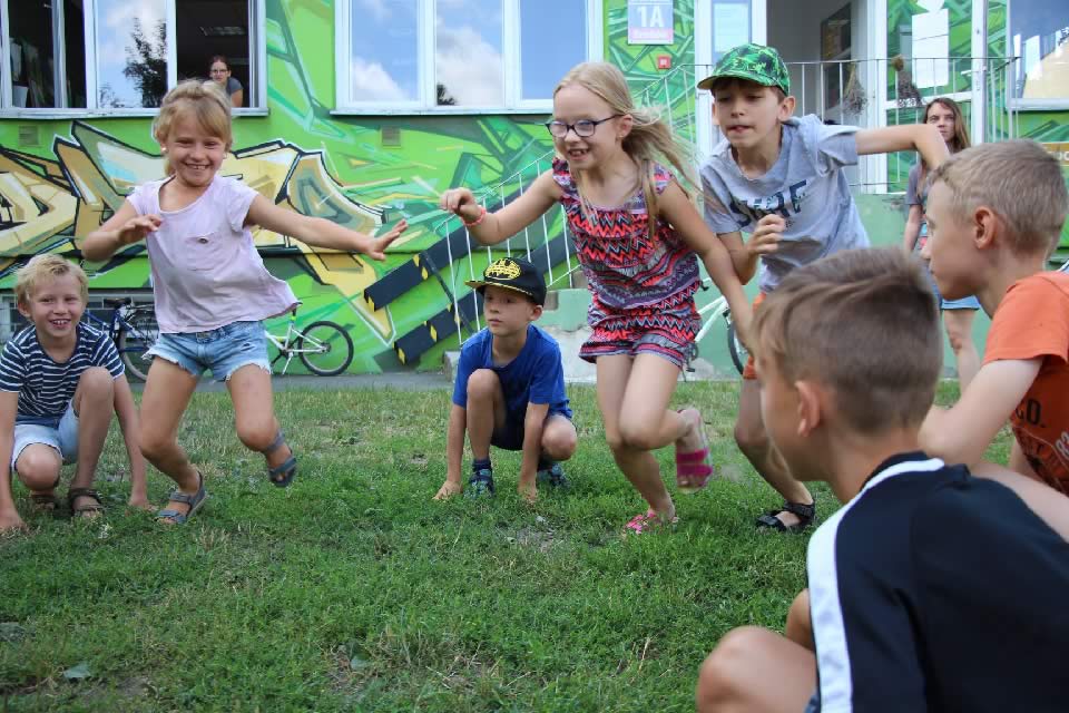 Grupa uśmiechniętych dzieci bawiąca się na trawie