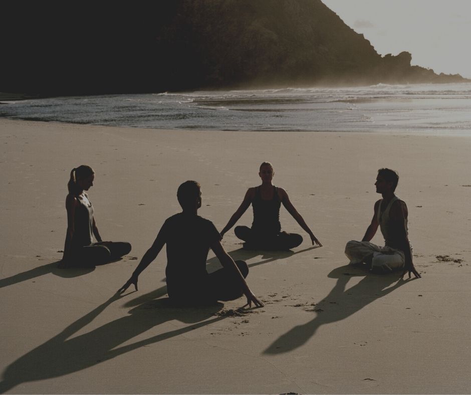 Cztery osoby siedzą na plaży w pozycji jogi. 